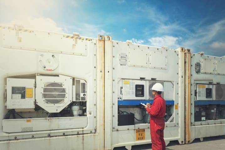 Service employee inspects container control panel and makes notes.