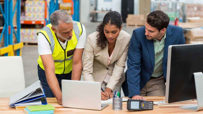 Drei Menschen stehen am Schreibtisch vor einem Laptop