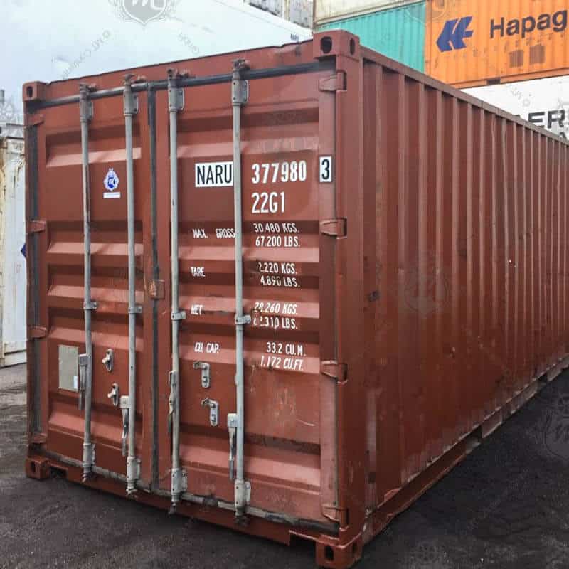 Ein brauner 20-Fuß-Seecontainer mit der Aufschrift "NARU 377980-3" steht im Vordergrund.