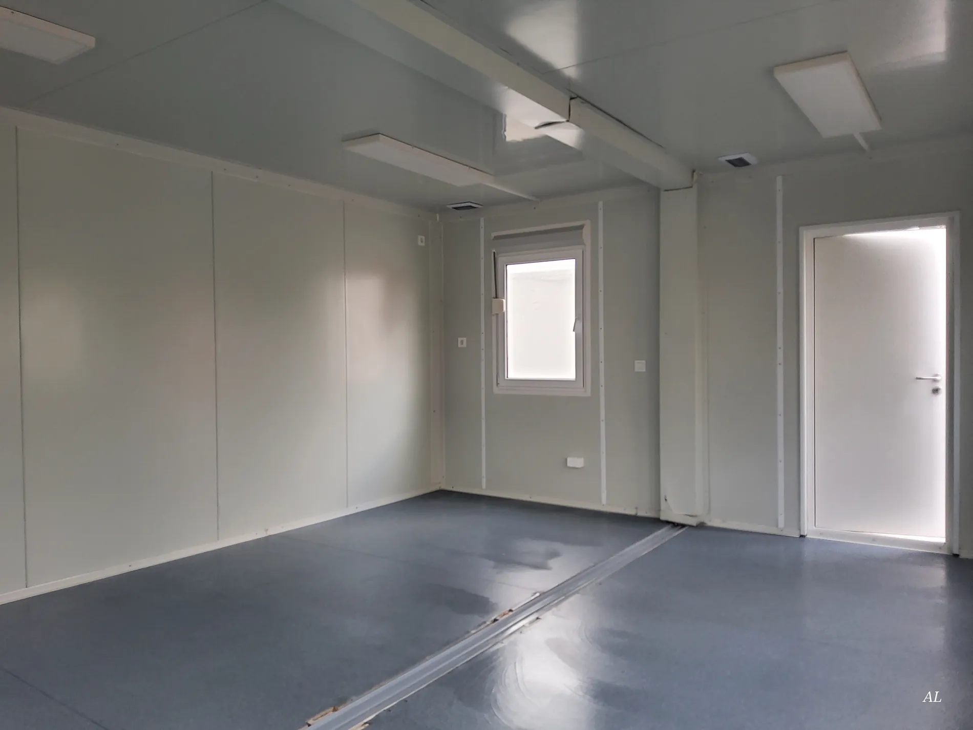 Leerer Büroraum im grauen Bürocontainer mit Fenster und Verbindungstür