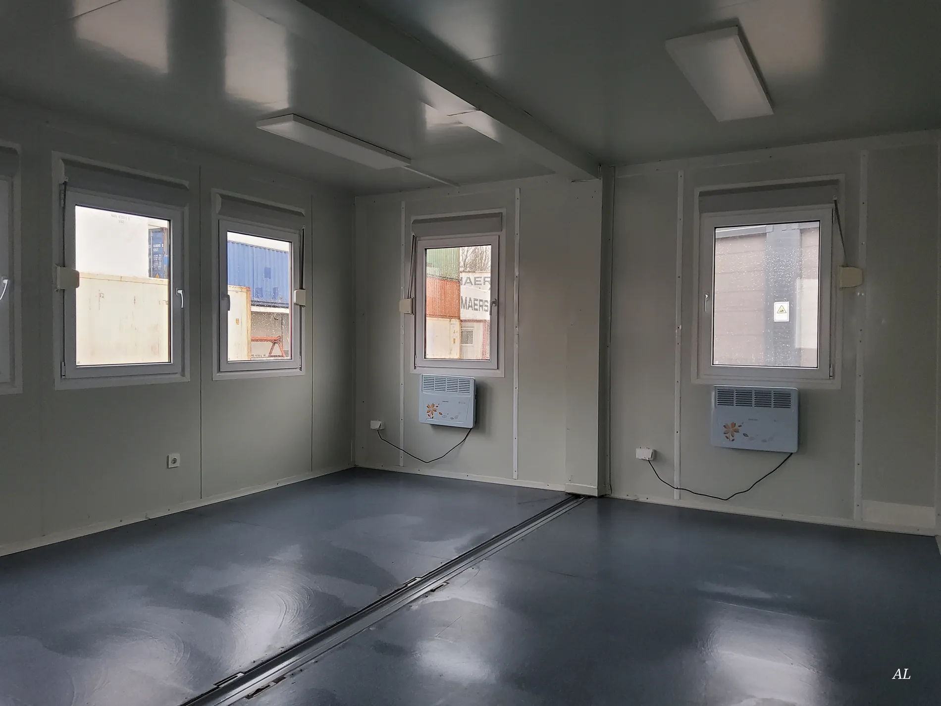 Innenraum einer grauen Bürocontainer-Doppelanlage mit vier Fenstern und zwei Elektroheizungen
